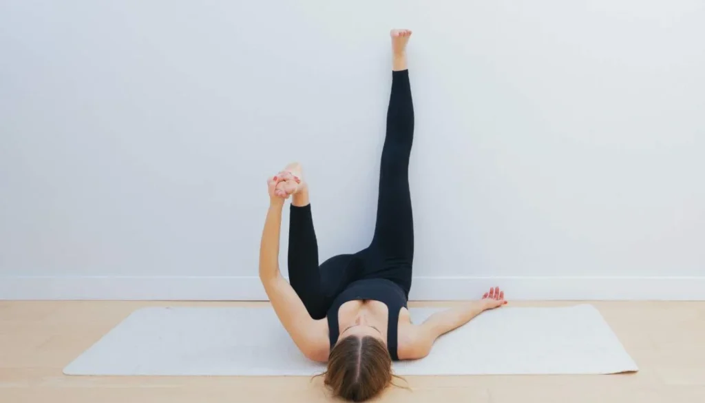 A lady lying on the floor and performs a Ardha Ananda Balasana (Half Happy Baby Pose)