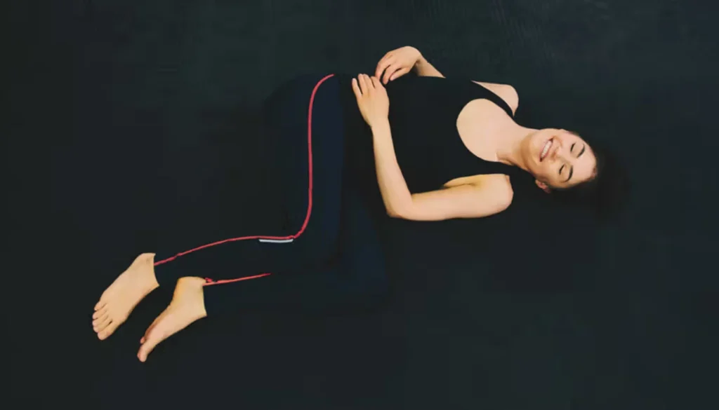 A lady laying on the floor and performs a Somatic External Hip Rotation