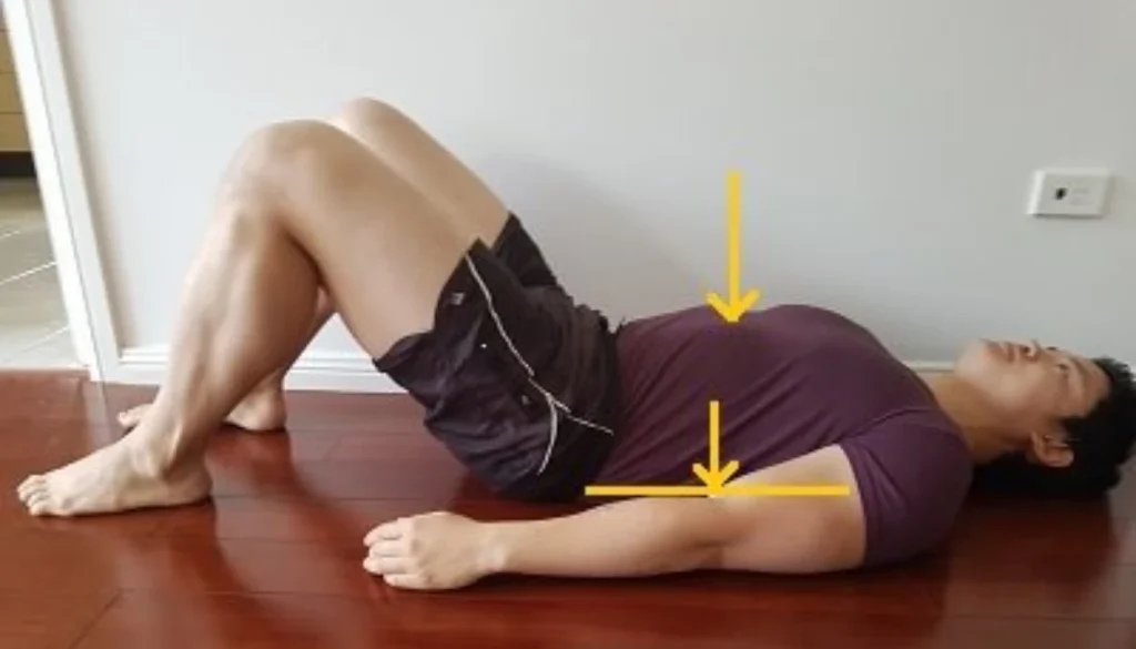 A man laying on the floor and performs a ribcage breathing